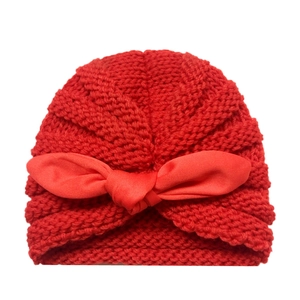 Close-up of red knitted baby hat featuring a large bow and soft textured weave