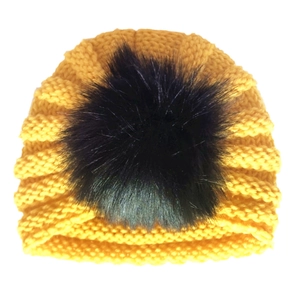Detailed close-up of yellow knit baby hat with thick texture and black faux fur pom-pom