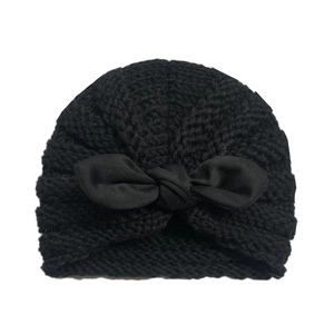 Close-up of black knitted baby turban beanie with large bow decoration on white background
