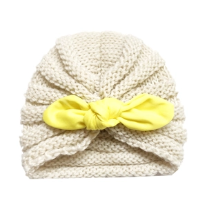 Cute knitted baby beanie in beige with a large yellow bow decoration on white background