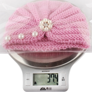 Pink knitted baby hat with pearls shown on a digital scale weighing 37.4 grams