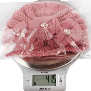 Detailed view of pink knitted baby hat with chiffon flowers and pearls on scale