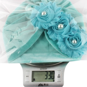 Detailed view of lightweight 33g baby velvet hat with flower and pearl on a scale