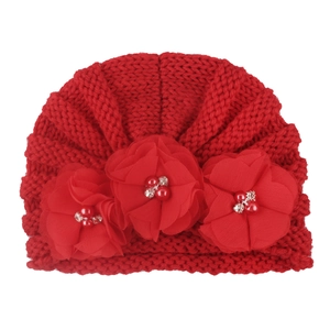 Close-up of baby red knitted turban hat with decorative mesh flowers and red pearls