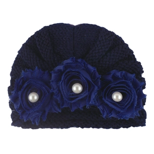 Detail of dark blue knit baby hat featuring ruffled texture and three fabric roses with pearls