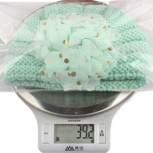 Detail view of a mint green knit baby hat with flower detail on weighing scale