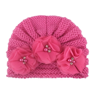 Detailed macro view of pink knitted baby hat with soft chiffon flowers and pearl accents