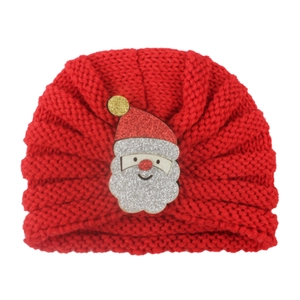 Détail du bonnet turban rouge tricoté pour bébé avec un écusson du Père Noël brillant