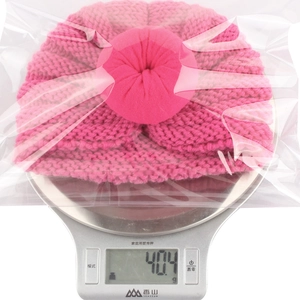 Pink knit baby hat with donut top decoration on scale weighing exactly 40.4 grams