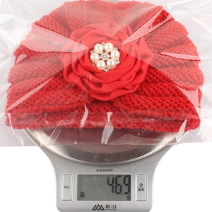 Détail du bonnet tricoté rouge pour bébé avec fleur en satin pesant 46,9g sur balance