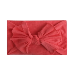 Close-up of soft coral nylon baby headband with a large bow and fine knitted texture