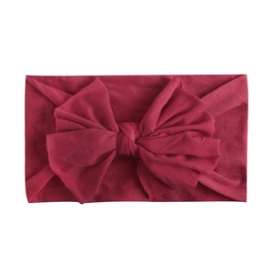 Detail of soft nylon baby headband with large wine red bow on white background