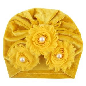 Detail of yellow velvet baby turban featuring three fabric flowers with center pearls
