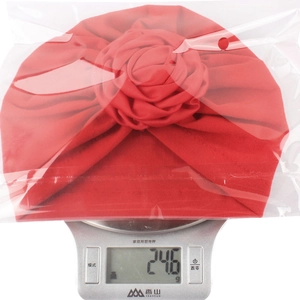Dettaglio del cappello turbante rosso per neonato che pesa 24,6g sulla bilancia di precisione