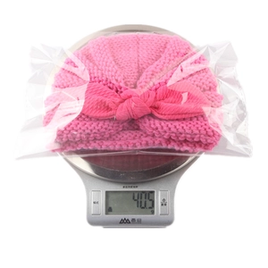 Macro shot of a pink knitted baby hat with rabbit ears on a digital scale for weight check