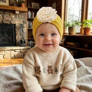 Detail of yellow knitted baby earflap hat with a large cream satin flower decoration