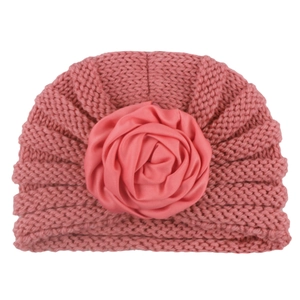 Detail of pink knitted baby turban hat featuring a large satin rose flower decoration