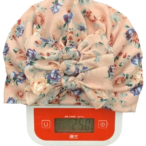 Dettaglio macro del turbante rosa a fiori per neonati che pesa 25 grammi sulla bilancia