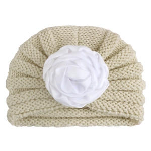 Macro detail of creamy white knitted baby turban hat with a large soft fabric flower