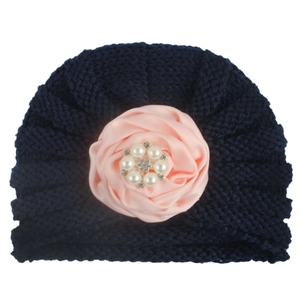 Détail d'un bonnet tricoté marine pour bébé avec rose en satin rose, perles et strass