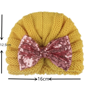 Detail of yellow knit baby hat with pink sequin bow and size dimensions 16x12.5cm