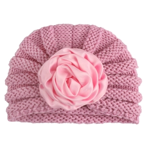 Detail of baby pink knit hat featuring a large satin rose flower for warm winter wear