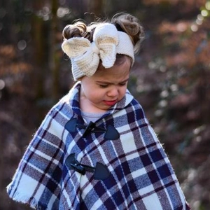 Détail d'un bandeau en maille blanche avec nœud et poncho à carreaux avec boutons en corne