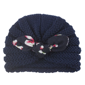 Detail of baby knitted turban hat in navy blue with a floral print bow knot decoration