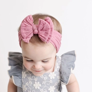 Gros plan d'un bandeau bébé en nylon rose poudré avec un grand nœud en jacquard doux