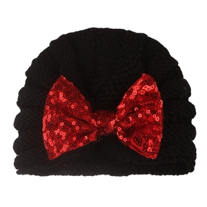 Knitted baby hat in black yarn featuring a large red sequin bow decoration