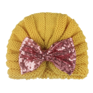 Knitted yellow baby winter hat with a decorative pink sequined bow on a white background