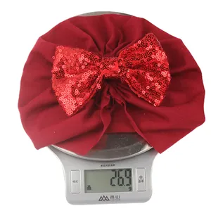 Weight display of red baby turban hat with sequin bow showing 26.9g on a digital scale