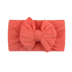 Détail d'un bandeau bébé en tricot rose corail avec un grand nœud papillon jacquard