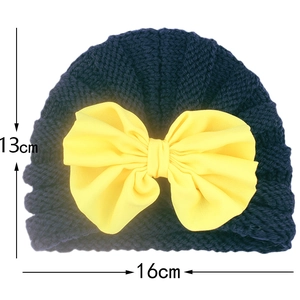 Detail view of navy blue knitted baby hat featuring a large yellow chiffon bow decoration