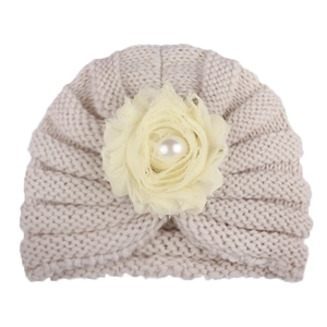 Détail du bonnet tricoté pour bébé avec fleur en mousseline et perle sur tissu beige