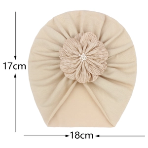 Dettaglio del turbante beige per neonati in maglia morbida con fiore e perla bianca