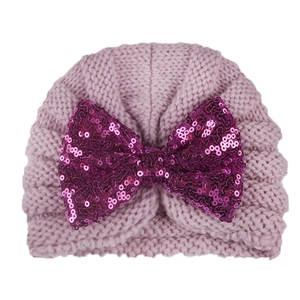 Close-up of knit baby beanie with a large purple sequined bow and ribbed texture