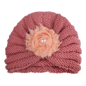 Détail de bonnet tricoté pour bébé avec fleur en mousseline rose et perle centrale