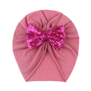 Macro view of a baby turban hat featuring a large pink sequin bow and pleated fabric