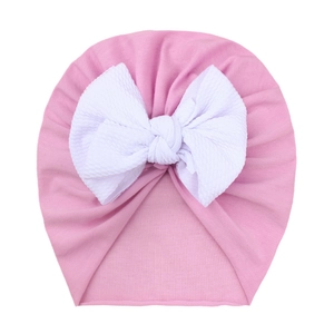 Detail of baby pink beanie with a large white waffle texture decorative bow
