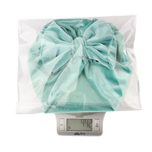 Detailed weighing of a mint green velvet baby turban hat with a large bow in packaging
