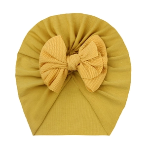 Detailed texture of ginger yellow ribbed knit baby hat with a large bow decoration