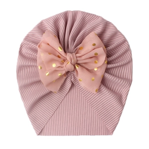 Detail of pink ribbed baby turban hat featuring a gold polka dot bow decoration