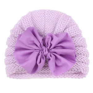 Close-up of a lavender knit baby hat featuring a large decorative dark purple fabric bow