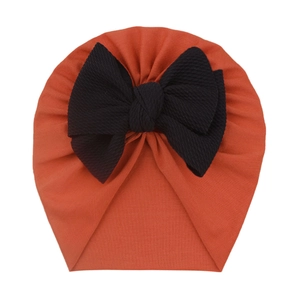 Detail of baby turban hat with a large black textured bow on caramel knit fabric