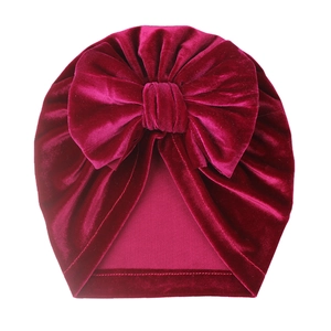 Detail of baby velvet turban hat in magenta featuring a large bow and soft pleated texture