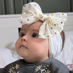 Détail d'un bandeau blanc pour bébé avec un grand nœud en dentelle à pois dorés sur nylon