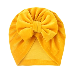 Detail view of ginger yellow velvet baby beanie with a large decorative bow and soft texture