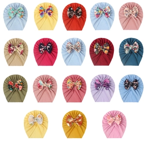 Collection of 18 soft baby turban hats with large bows in various solid colors and floral prints