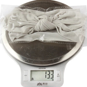 Detailed view of grey soft nylon baby headband with bow weighed at 13.3g on scale